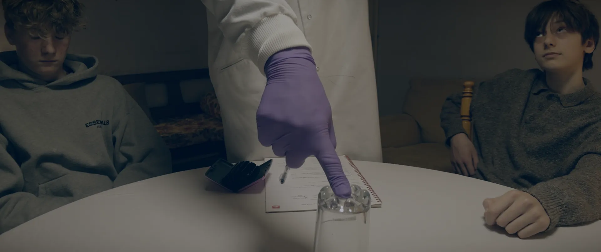 Dr Aldiss's gloved hand placing a glass on the table